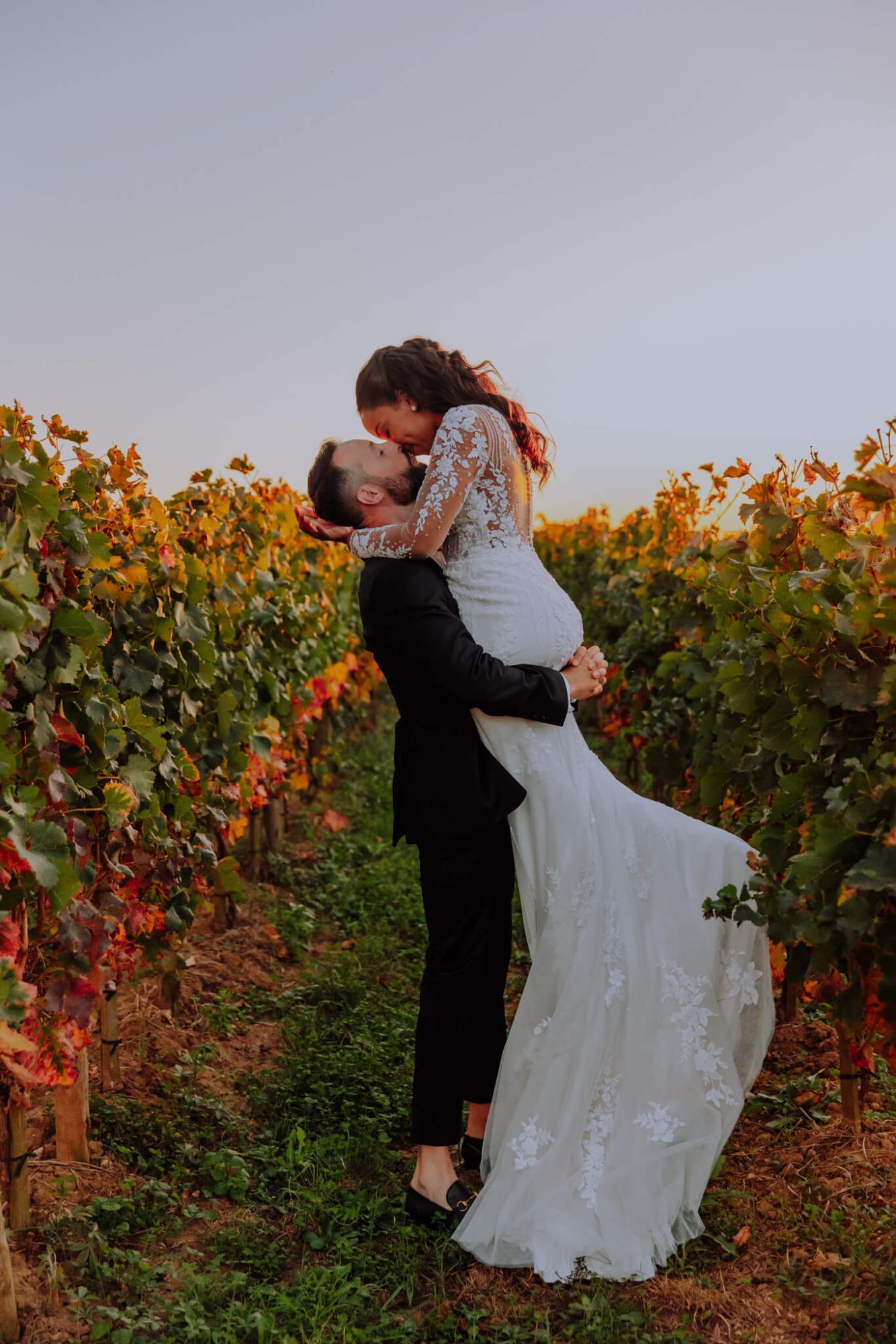 Le marié porte la mariée et l'embrasse.Ils sont au milieu des vignes